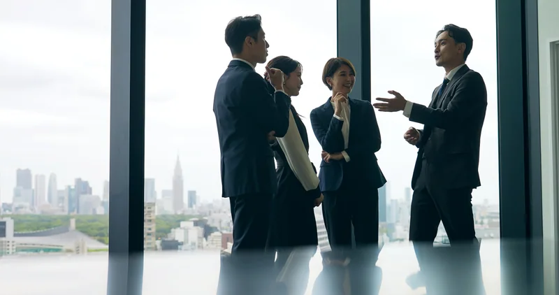 窓辺で和やかに話す4人のビジネスパーソンのイメージ